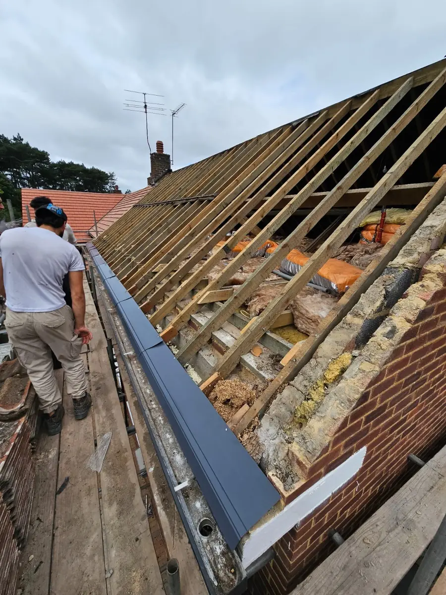 Roofer at the ridge of a roof stripped to the rafters