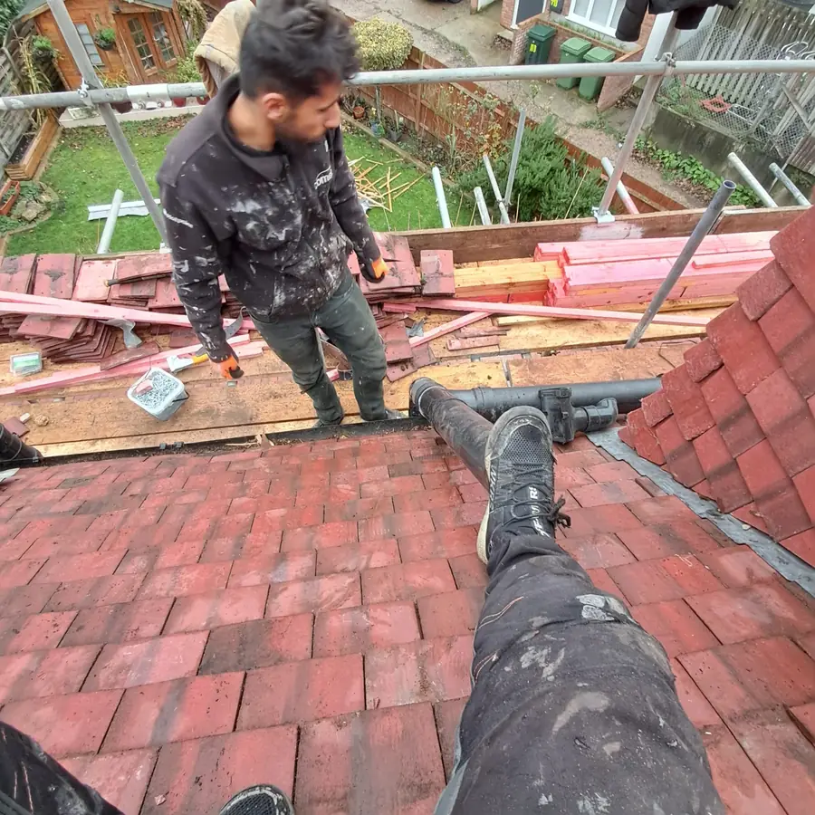 Roofer stripping old red tiles off a roof