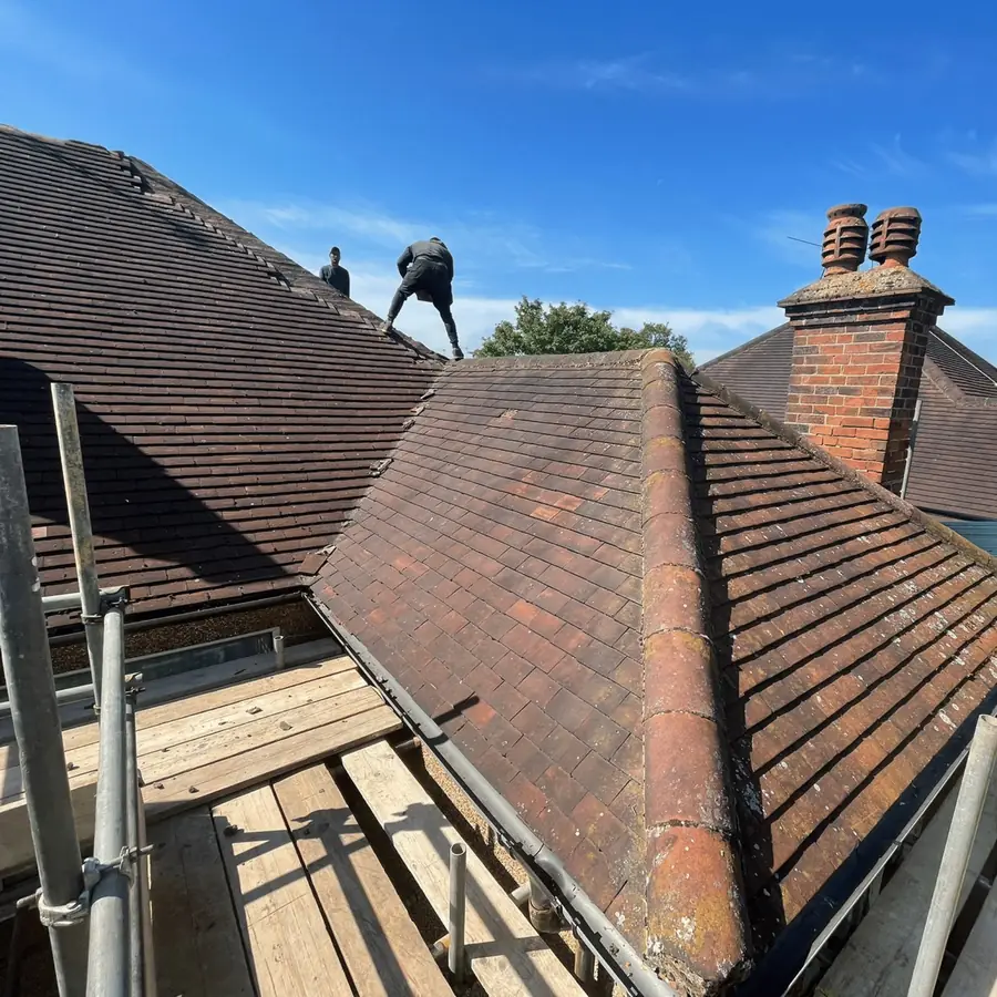 Worn tiled hip roof before work, roofer on the ridge